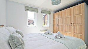 A bedroom with a large bed, two windows with blinds, a wardrobe, and a hanging light fixture.