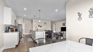Une cuisine moderne avec des meubles blancs, un coin repas doté d’une table en marbre et un espace de vie comprenant un canapé et une table basse.