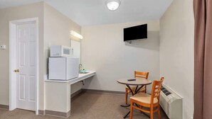 Ein kleines Zimmer mit Küchenzeile, einem Esstisch mit Stühlen, einem an der Wand befestigten Flachbildfernseher und einer Tür.