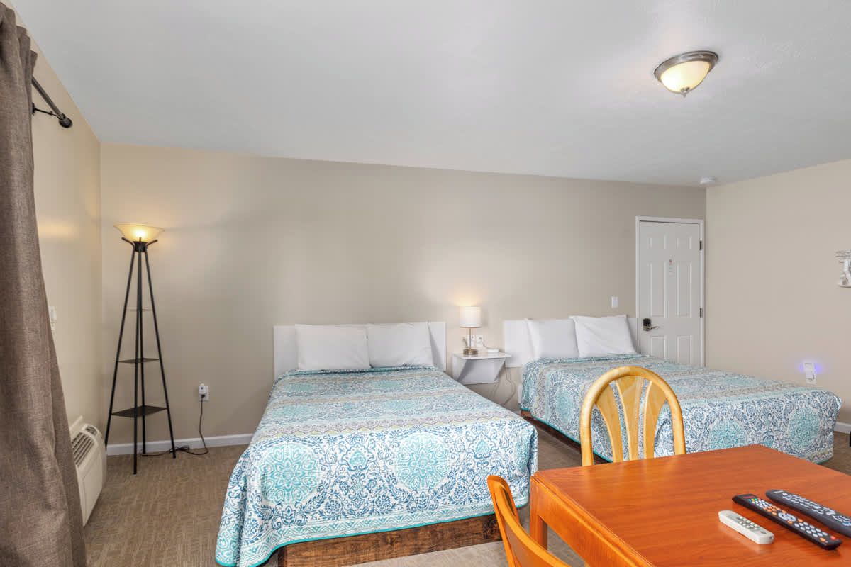 Une chambre d’hôtel avec deux lits, une table en bois et une lampe sur pied.