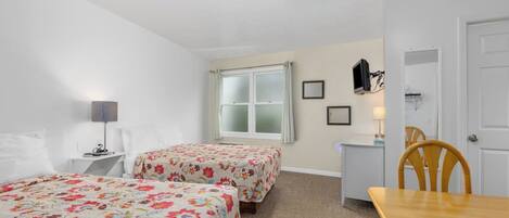 A room with two beds, a desk, a chair, and a television.