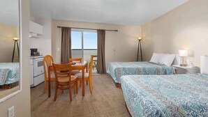 Ein Hotelzimmer mit zwei Betten, einem Esstisch mit Stühlen, einer Küchenzeile und einem großen Fenster mit Vorhängen.