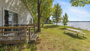 Una cabaña junto al lago con terraza de madera y mesa de picnic.