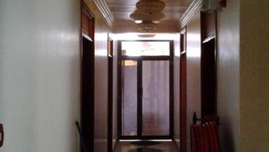 Um corredor com piso estampado, teto com luminária central e porta no final.