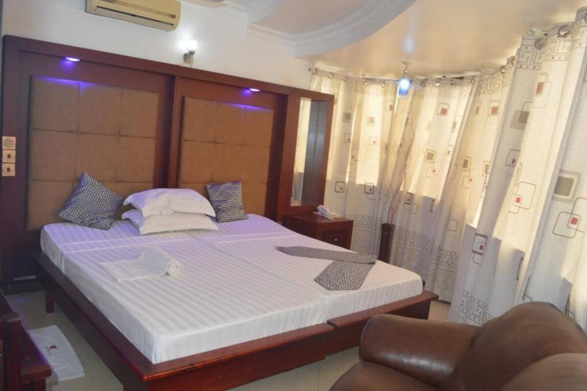 Une chambre d’hôtel avec un grand lit, une tête de lit en bois, une table de chevet et un fauteuil en cuir marron.