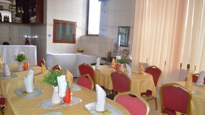 Restaurante com mesas redondas cobertas por toalhas amarelas, cadeiras vermelhas e guardanapos brancos.