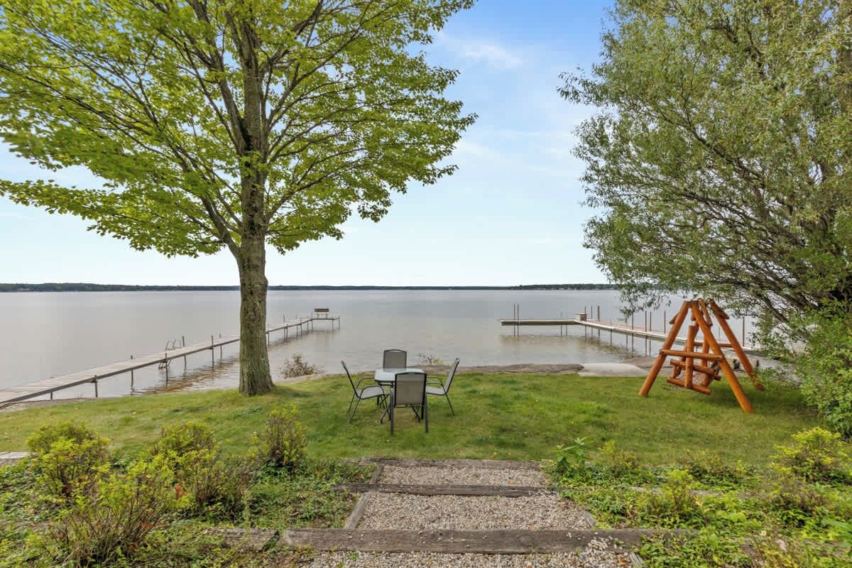 A lakeside patio with a table and chairs, a swing set, and a dock extending into the water.