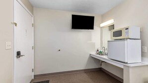 A small, clean bathroom with a toilet, sink, and a mirror. A television is mounted on the wall above the mirror.