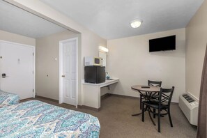 Una habitación de hotel con cama, escritorio con microondas, televisor y una silla.