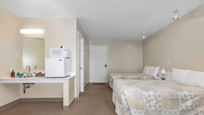 Habitación de hotel con kitchenette, dos camas, baño y puerta que da a otra habitación.