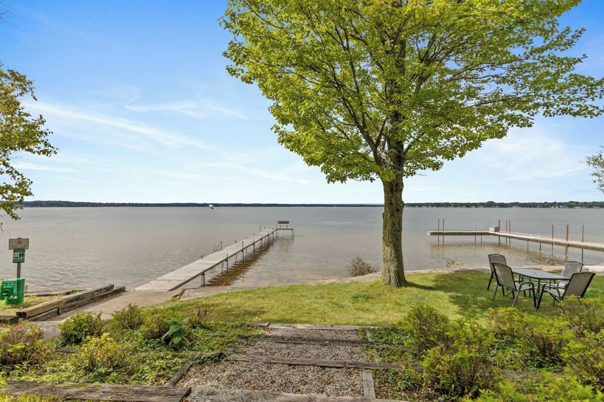A lakeside park with a dock extending into the water, a picnic table, and a tree.