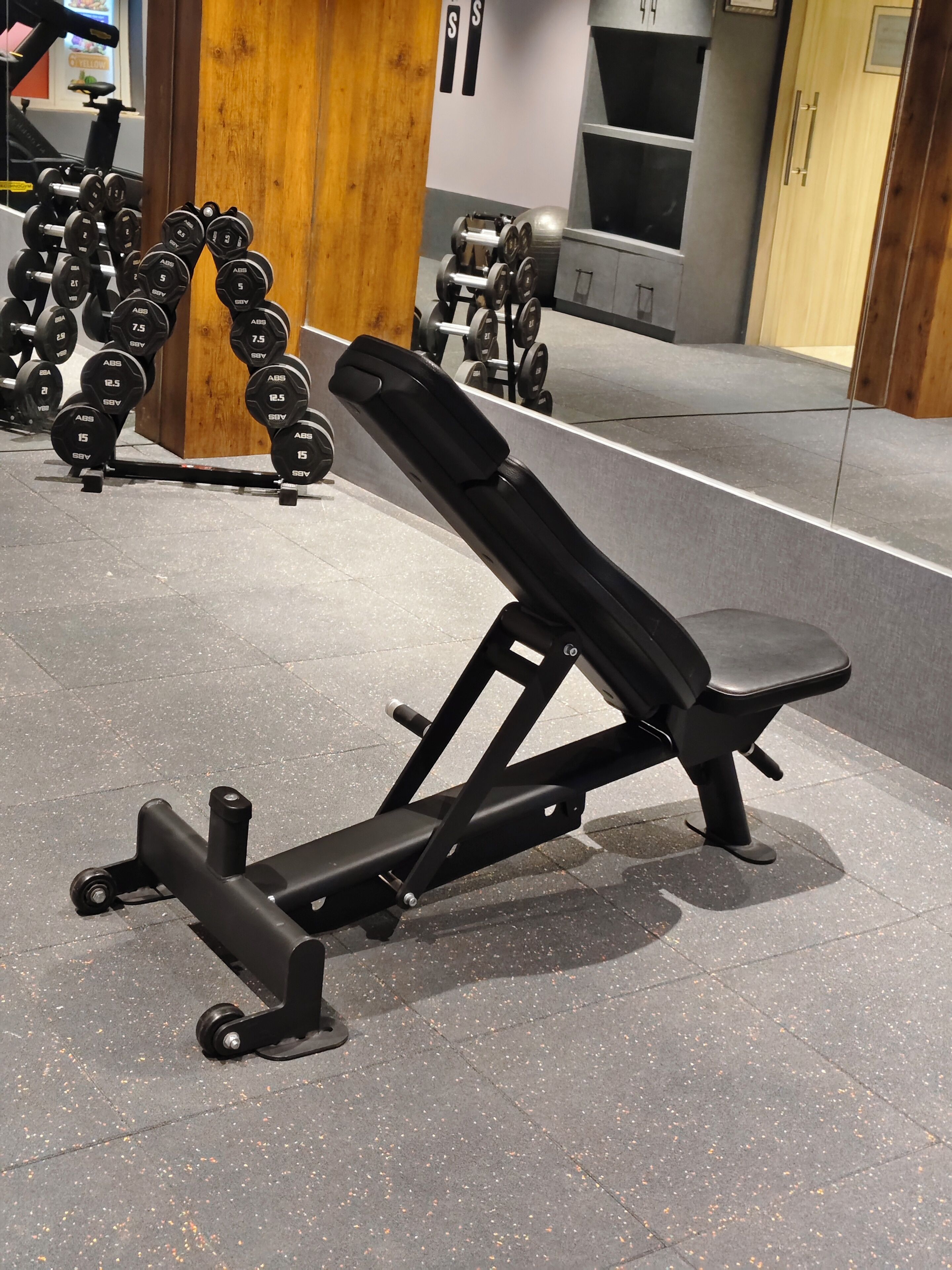 Máquina de press de banca en un gimnasio, con apilamientos de pesas y un espejo.