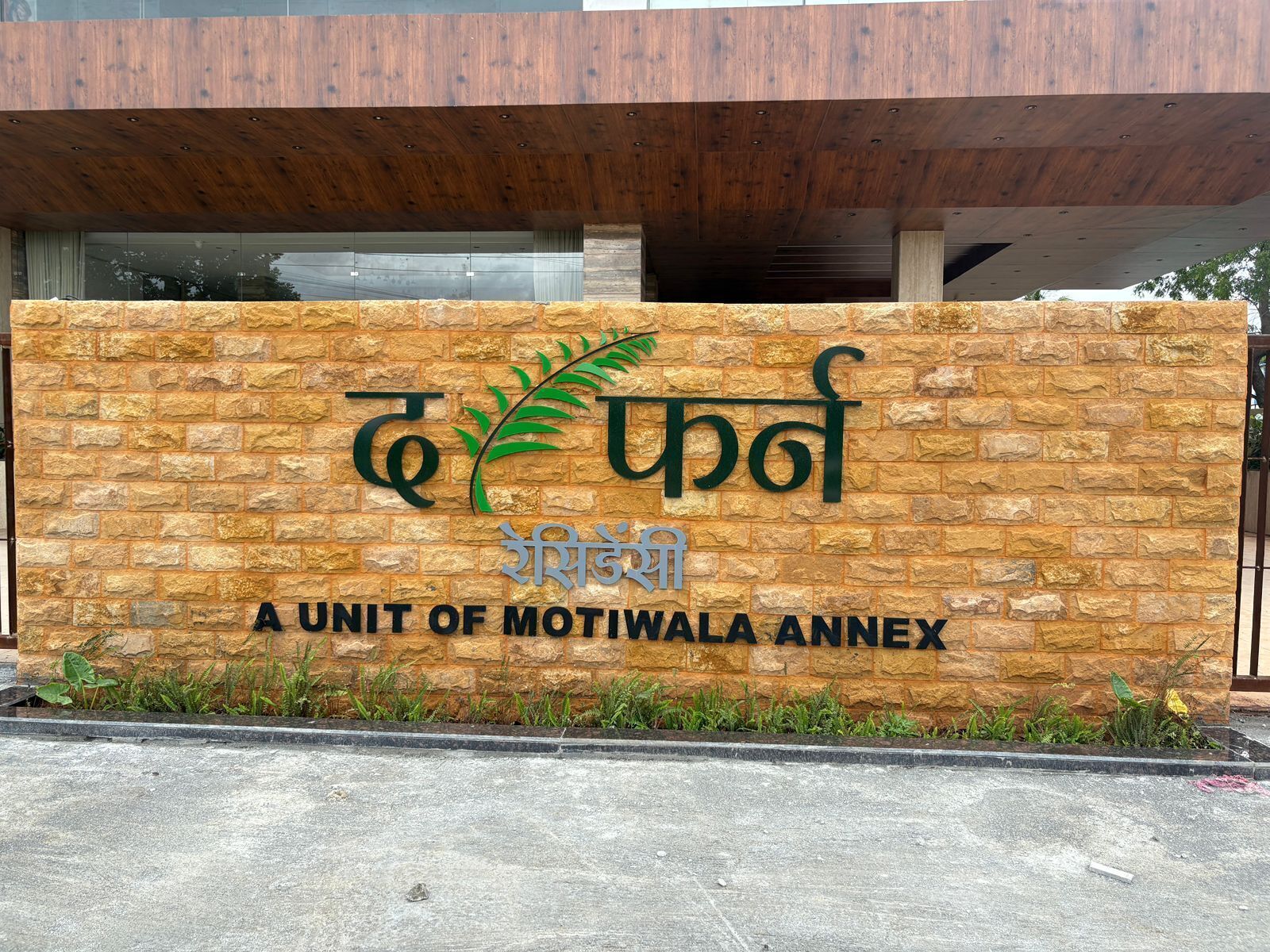 A sign for a unit of Motiwala Annex with a stone wall and a wooden overhang.