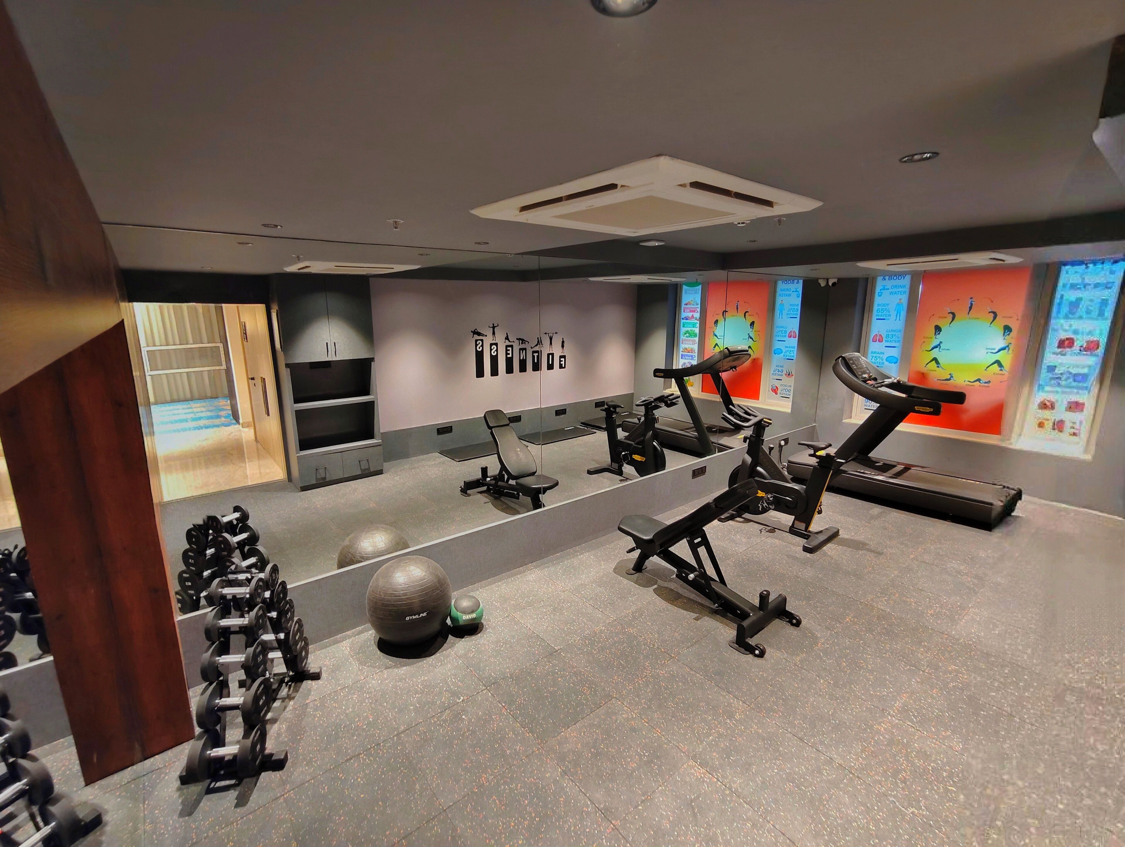 A modern gym with exercise equipment, a mirrored wall, and informational posters.