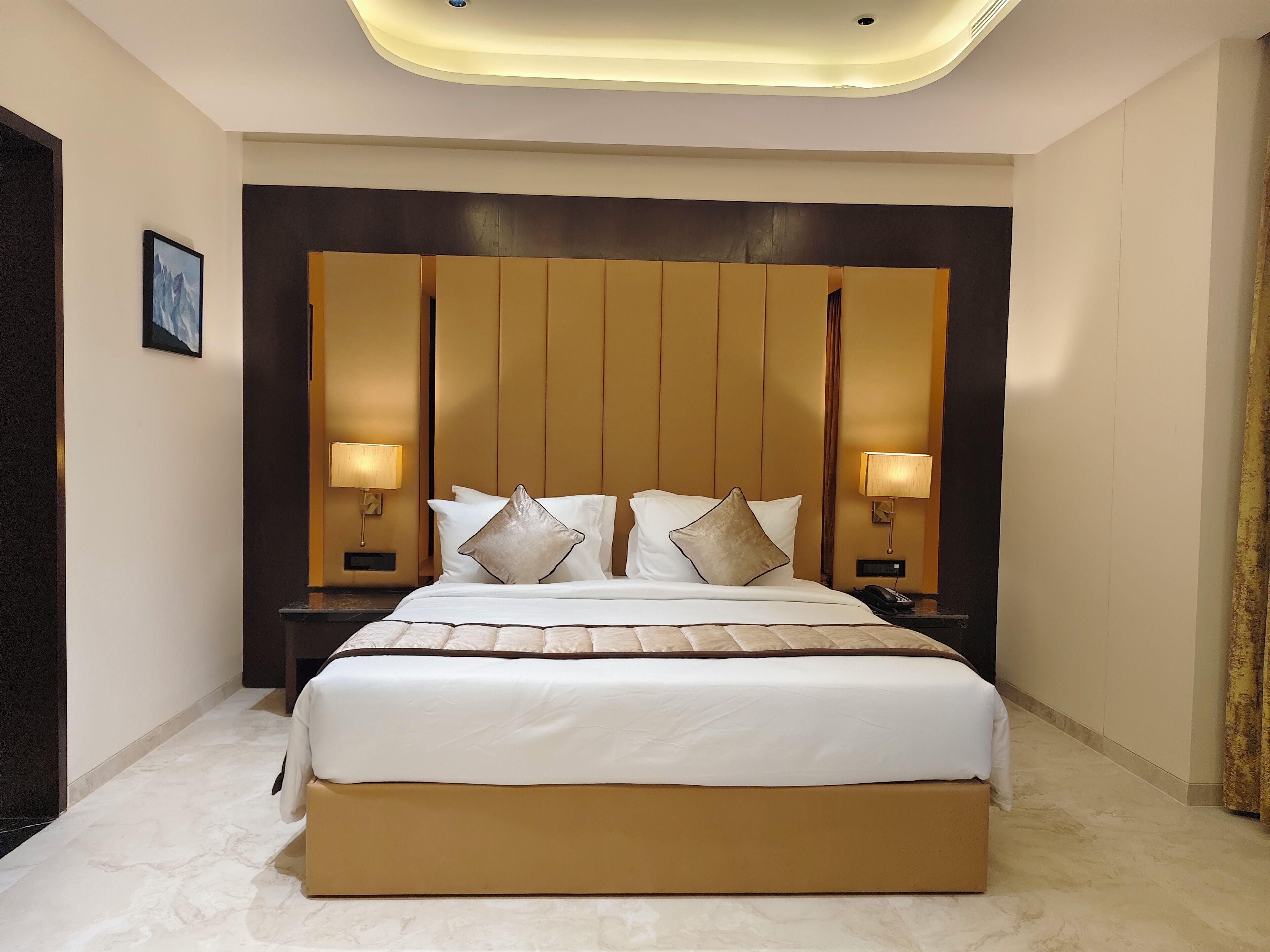 Una habitación de hotel con una cama grande, dos lámparas de noche, un espejo grande sobre la cama y un cuadro en la pared.