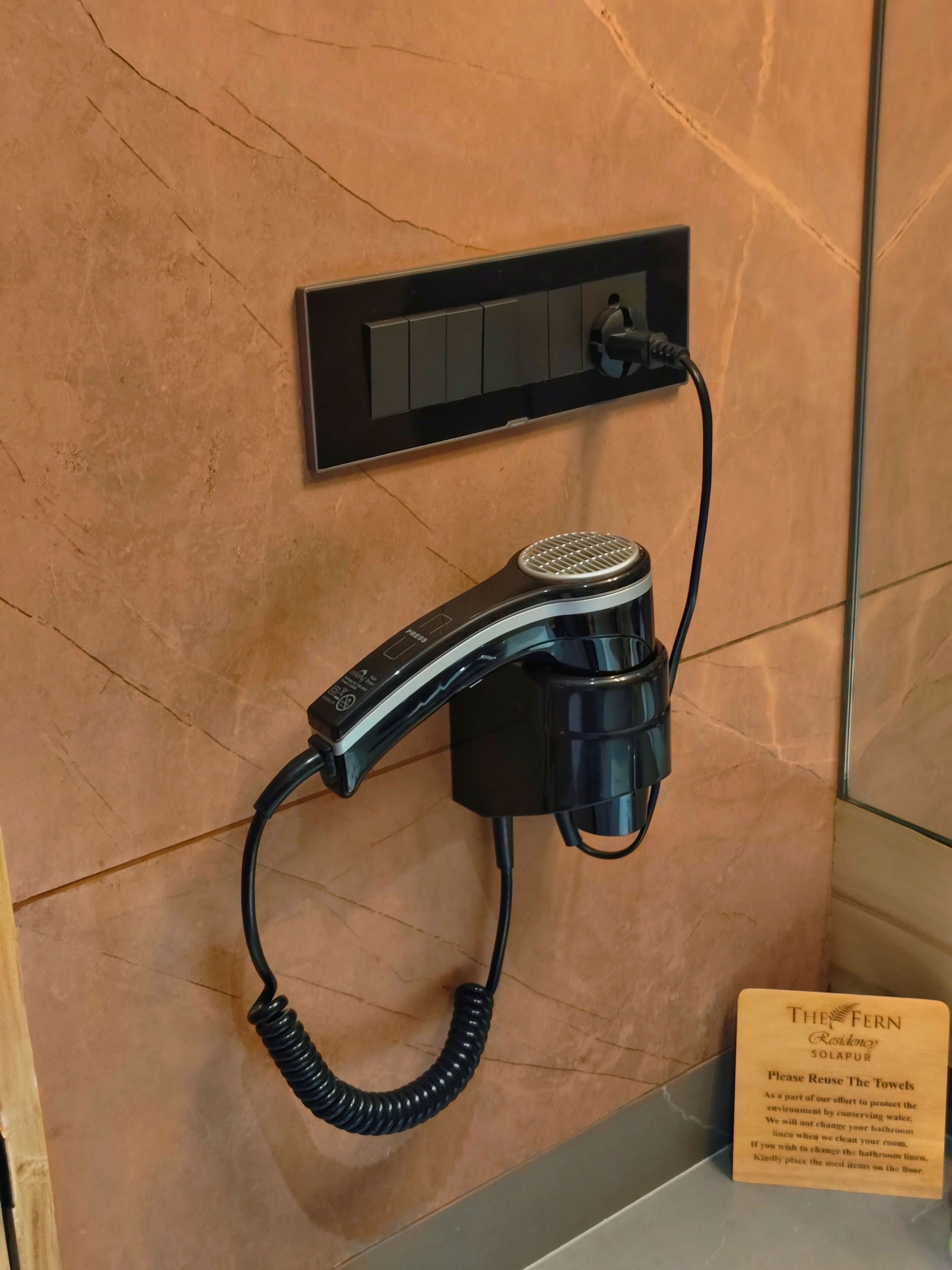 A hair dryer mounted on a wall with a sign below instructing to reuse towels.