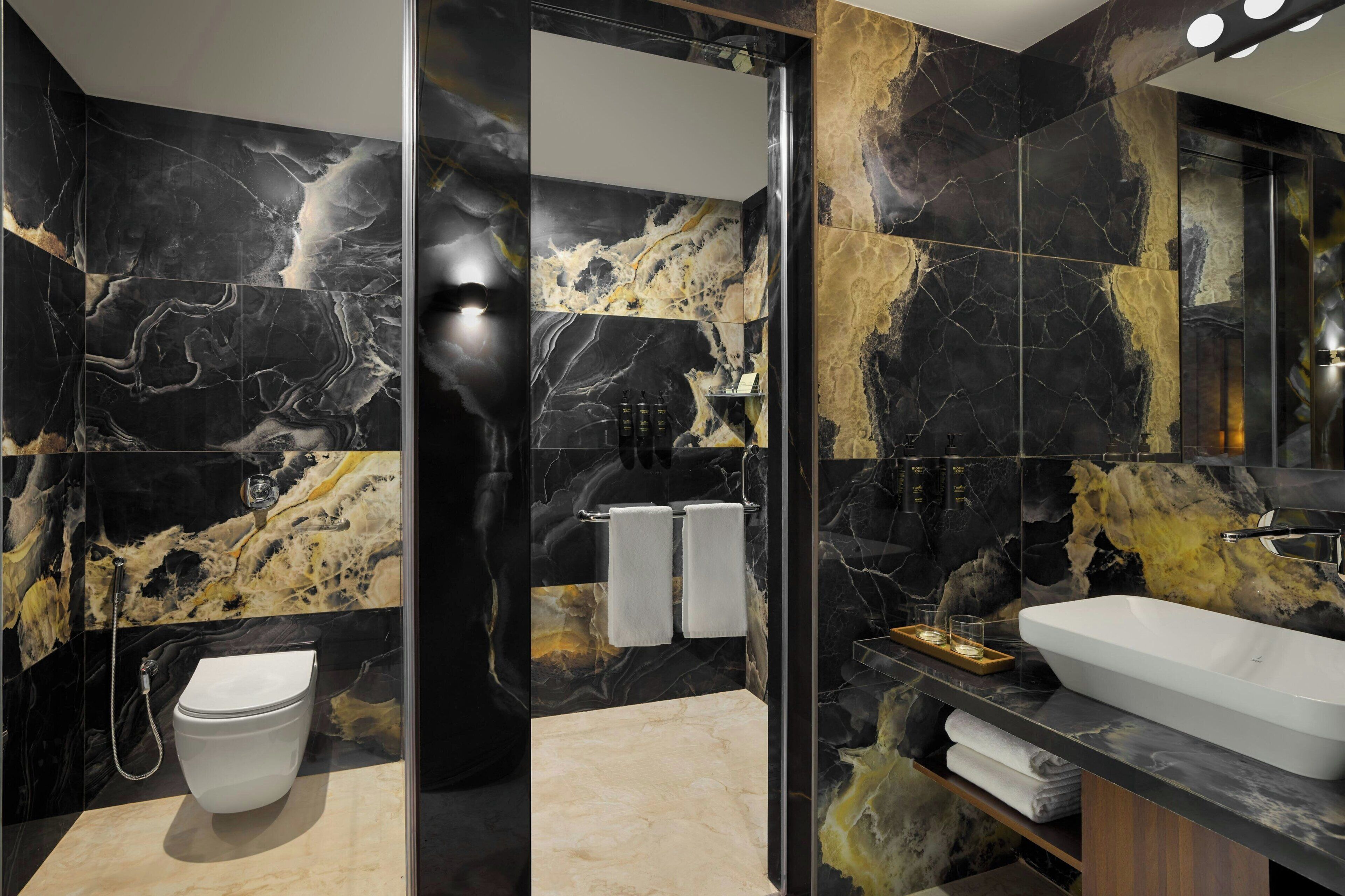 A modern bathroom with a black and gold marble design, a white toilet, and a large sink.