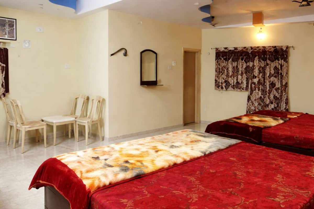 Habitación de hotel con dos camas, un escritorio con sillas, un espejo, una puerta y un ventilador de techo.