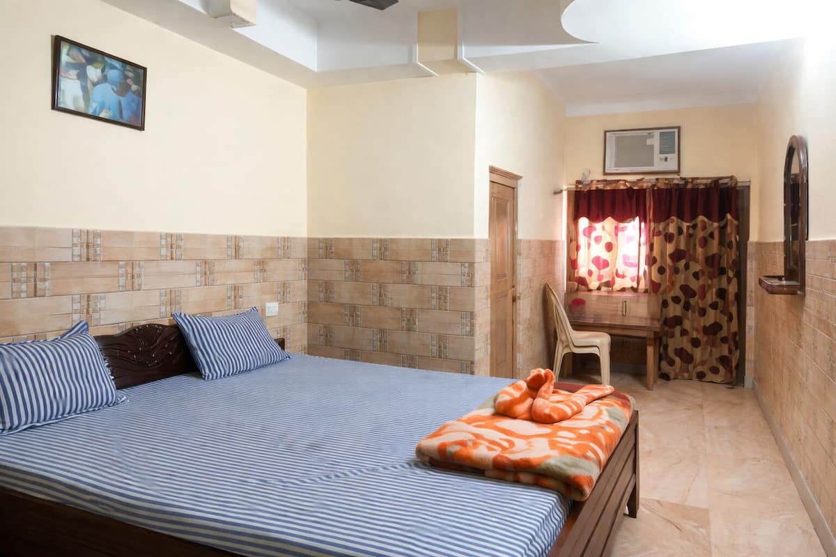 Un dormitorio con cama, una silla, zona de ducha y aire acondicionado instalado en la pared.