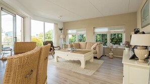 Amplia sala de estar con un gran ventanal, un sofá, una mesita de centro y sillones de mimbre.