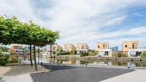 Un paseo fluvial con edificios modernos, una zona de estar cubierta y una masa de agua tranquila.