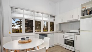 A modern kitchen with white cabinetry, a dining table with chairs, and a view of trees through large windows.