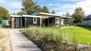 A modern house with a glass conservatory, a paved driveway, and a well-maintained lawn.