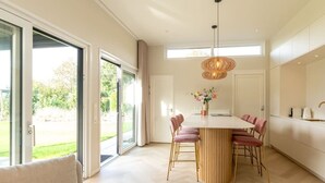 A modern kitchen with a central island, large windows, and a dining area with chairs.