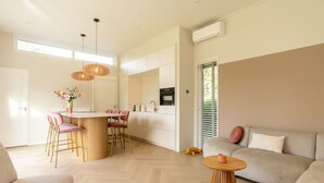 A modern living room with a sofa, a dining area with a round table, and a kitchen visible in the background.