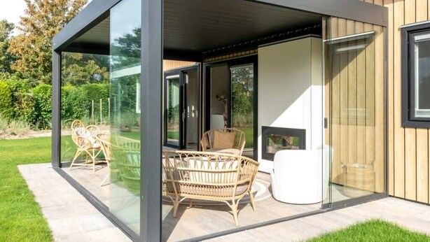 A modern house with a glass-enclosed patio area featuring outdoor furniture.