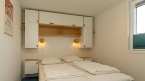 A small, neatly arranged bedroom with a single bed, a wooden headboard, and a white wardrobe with two wall-mounted lights.
