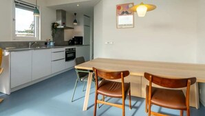 A modern kitchen with a dining area, including a wooden table and chairs, a window, and a pendant light.
