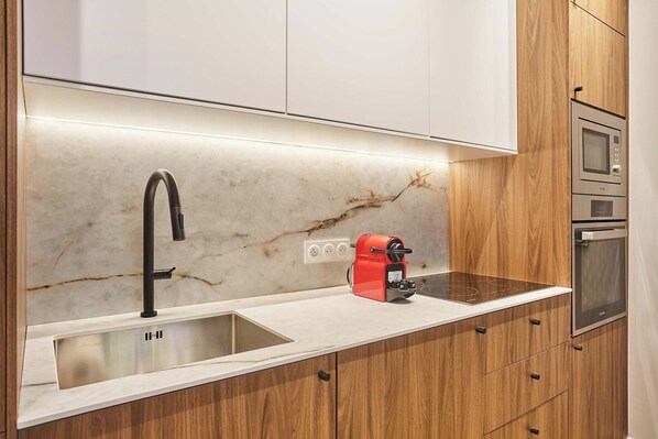 A modern kitchen with a marble countertop, a black faucet, a red coffee machine, and built-in ovens.
