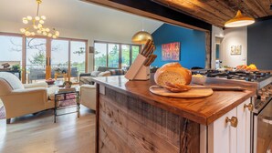 Una cocina moderna con una isla de madera, una zona de comedor con sofá y grandes ventanales con vistas al exterior.