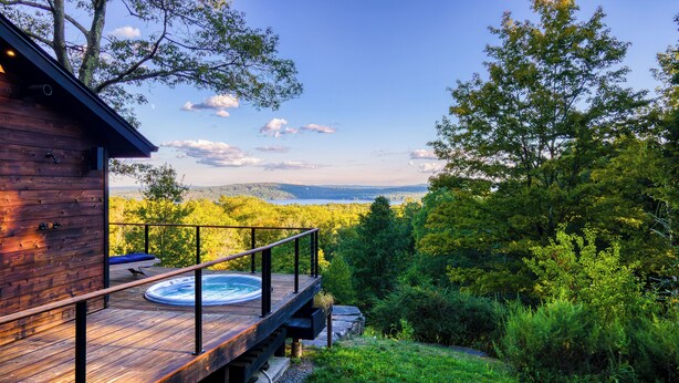 Una terraza de madera con un jacuzzi, con vistas a un bosque y un lago.