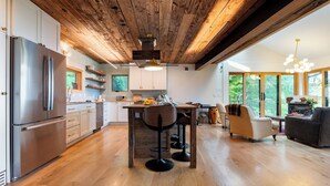 Una cocina moderna con vigas de madera, un refrigerador de acero inoxidable y un comedor con taburetes de bar.