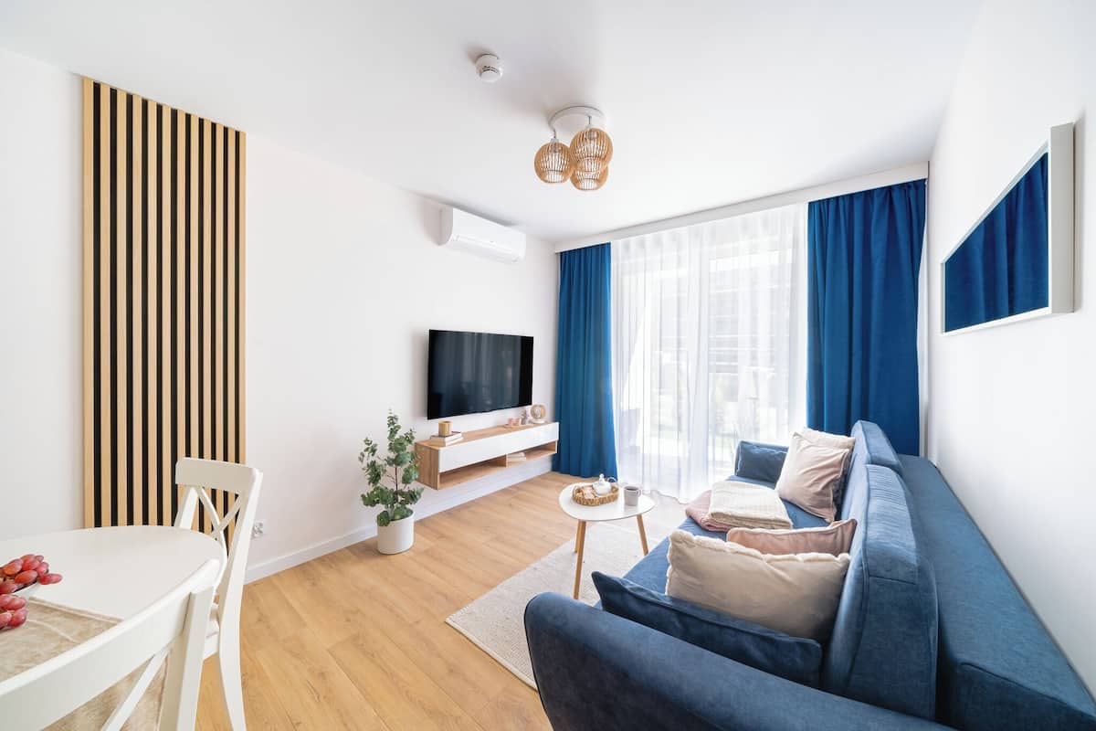 A modern living room with a sofa, a TV, a dining table with fruits, and a potted plant.