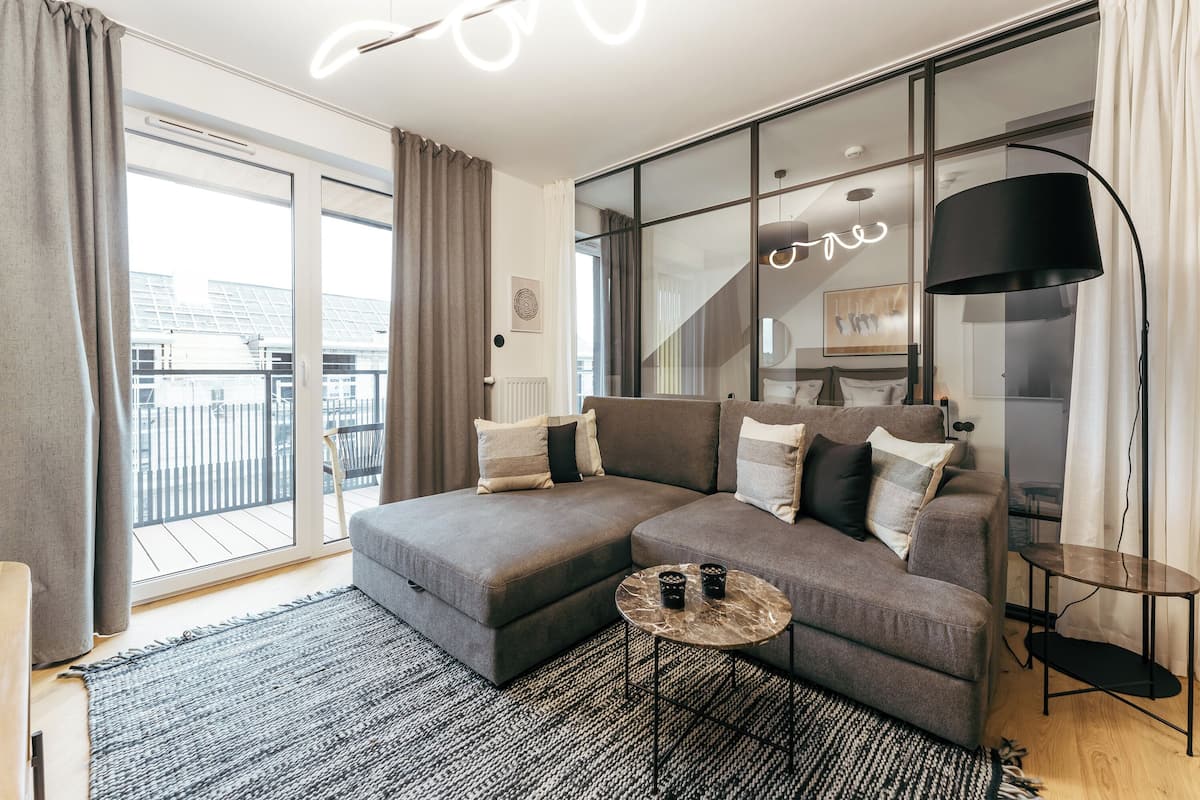 A modern living room with a grey sectional sofa, a small round table, and a large window with curtains.