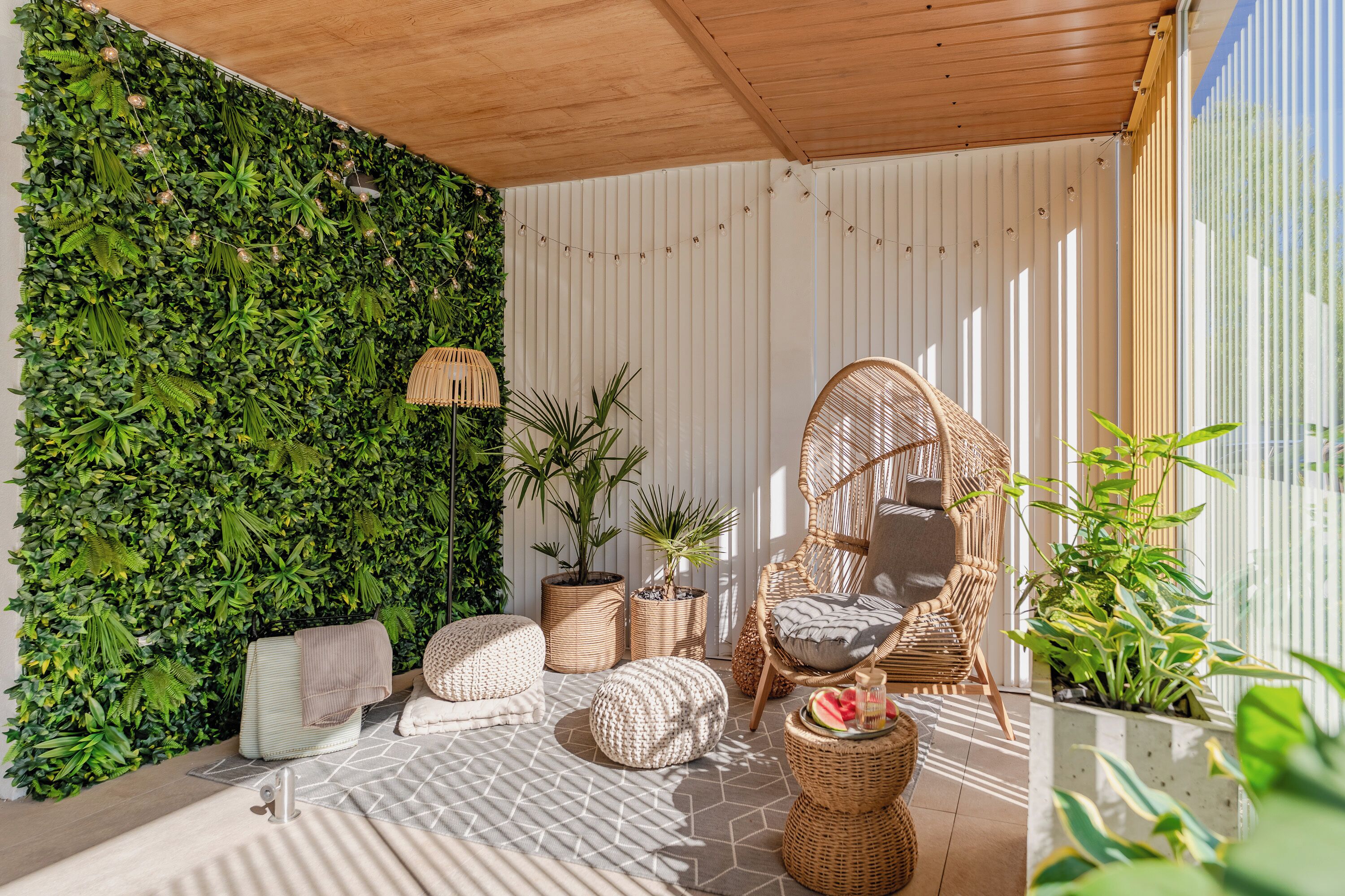 Een knus buitgedeelte met rieten meubels, een groene wand en potplanten.