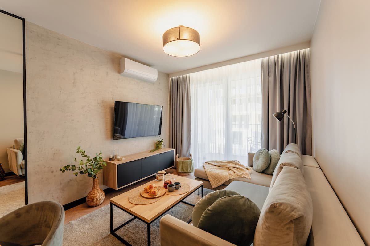 A modern living room with a flat-screen TV, a sofa, a coffee table, and a large window with curtains.