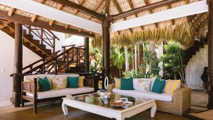 Amplia sala de estar con techo alto, una escalera y exuberantes plantas tropicales.