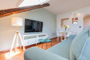 A modern living room with a flat-screen TV, white furniture, and a wooden ceiling beam.