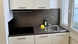 A small kitchen with white cabinets, a black countertop, a stainless steel sink, and a window with a view of buildings outside. - Romulus House (Milano)
