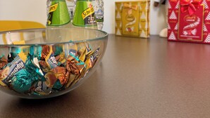 A bowl filled with wrapped candies and two bottles of Schweppes Limonade on a wooden table. - Romulus House (Milano)