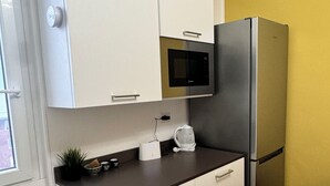 A compact kitchen with white cabinets, a stainless steel refrigerator, a microwave, and a coffee maker on the countertop. - Romulus House (Milano)