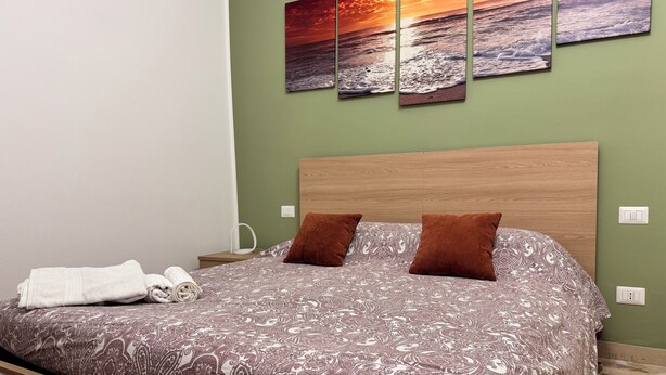 A neatly made bed with a patterned bedspread, two brown pillows, and a white towel on the side. - Romulus House (Milano)