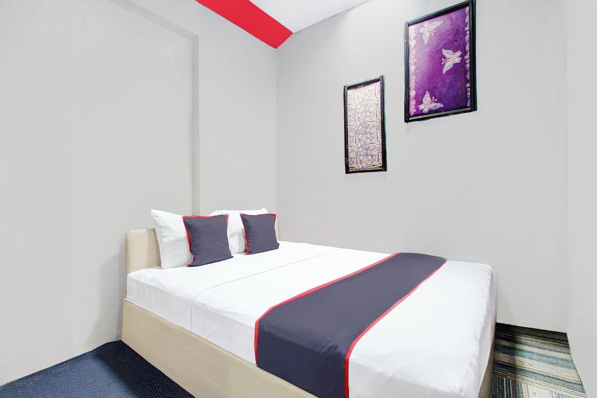 A hotel room with a bed, white walls, and a red accent on the ceiling. There are two framed artworks on the wall.