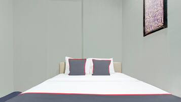 Cama bem arrumada com roupa de cama branca e cinza, dois travesseiros com detalhes vermelhos e um quadro na parede.