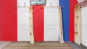 A room with a red, white, and blue wall design, featuring two white doors with beige curtains, a striped rug, and a framed picture above the doors. - Hotel O Putra Family Homestay Sikunir (Kejajar)