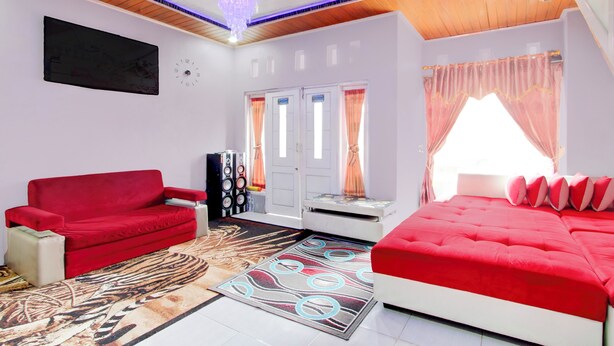A modern room with a red sofa, a white bed, a large rug, and a chandelier. - Hotel O Putra Family Homestay Sikunir (Kejajar)